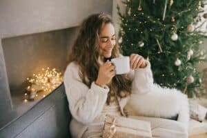 A woman smiling with a cup of coffee next to a Christmas tree